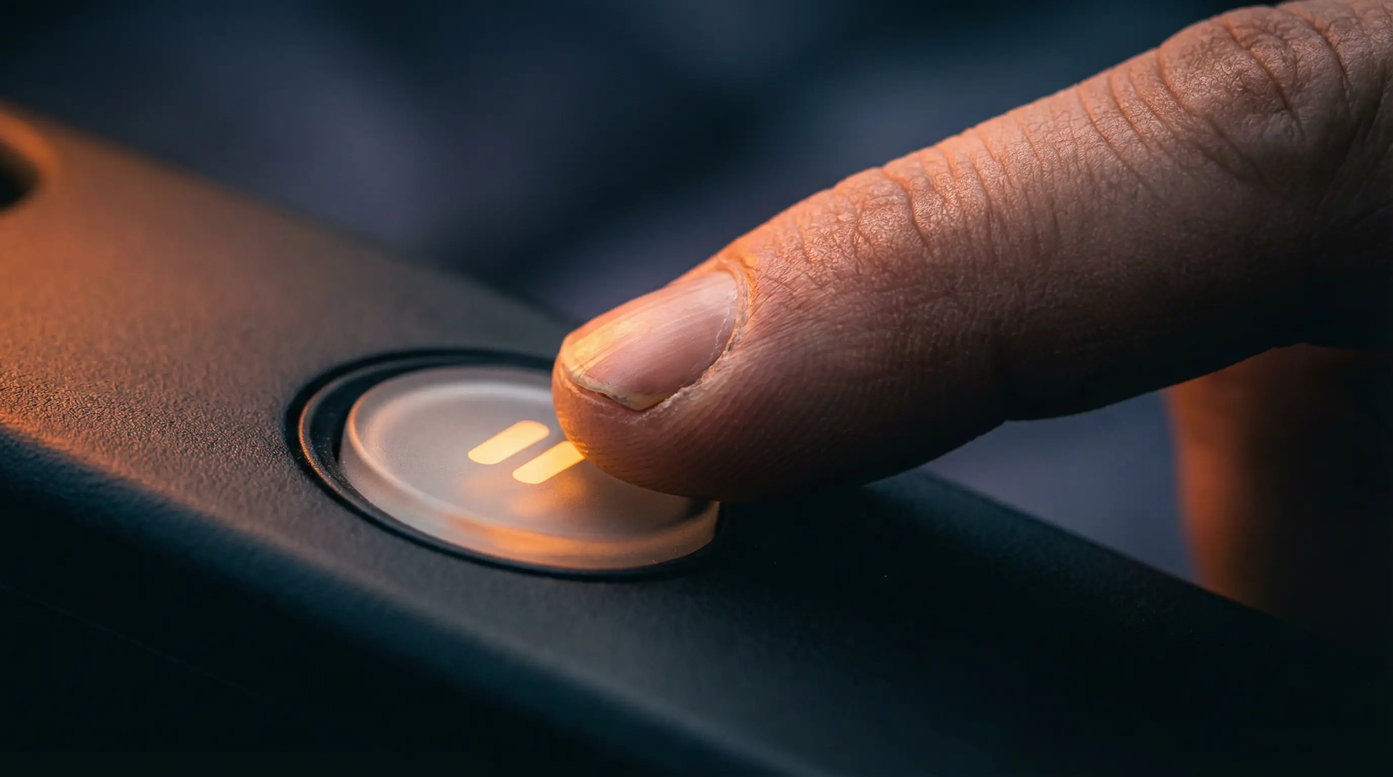Mano che preme un pulsante di pausa illuminato su uno sfondo scuro e sfocato