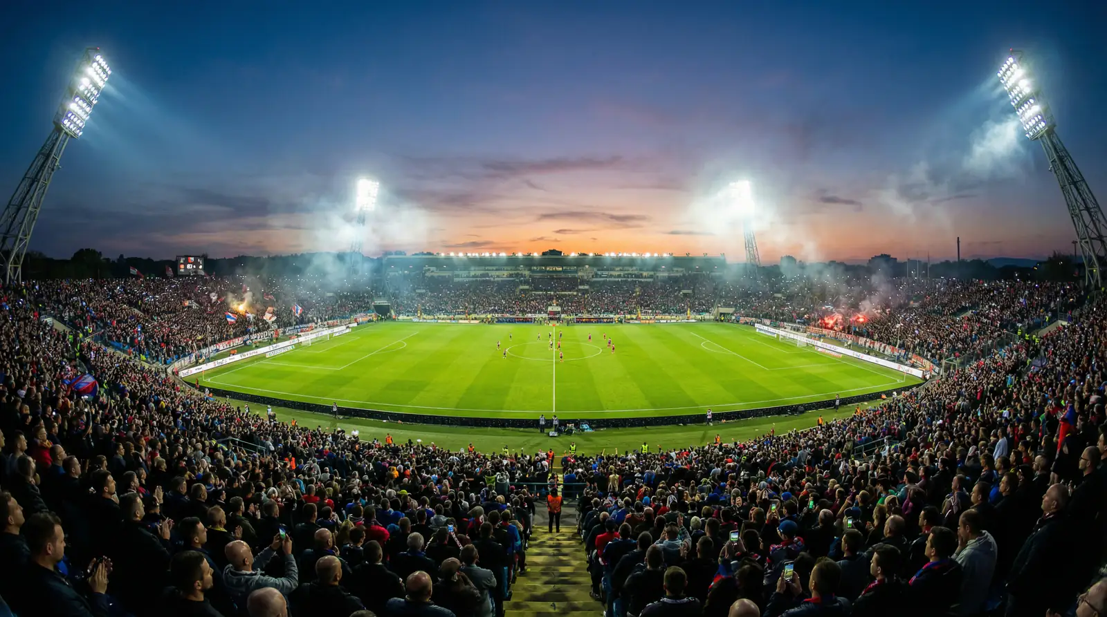 Stadio di calcio pieno di spettatori durante una partita serale con il campo illuminato dai riflettori