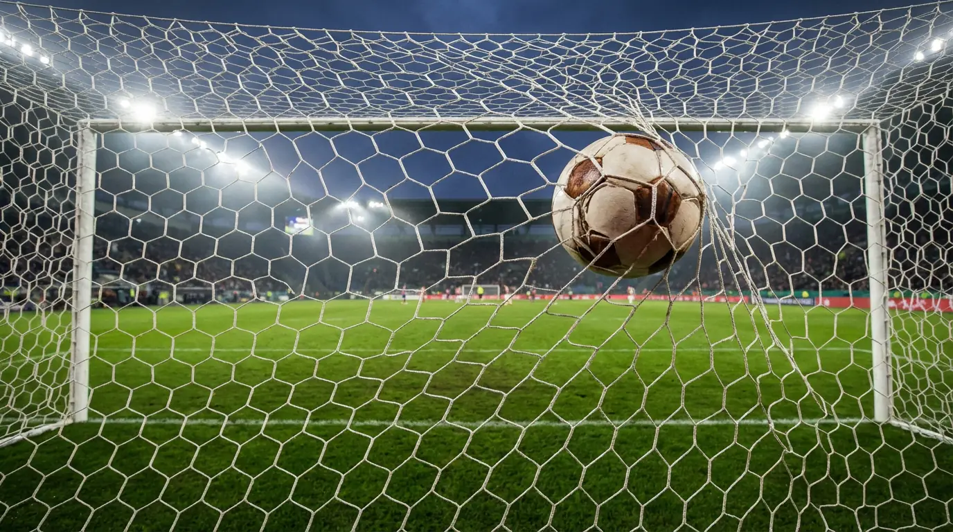 Rete di una porta da calcio vista da dietro con pallone che entra in rete sotto i riflettori